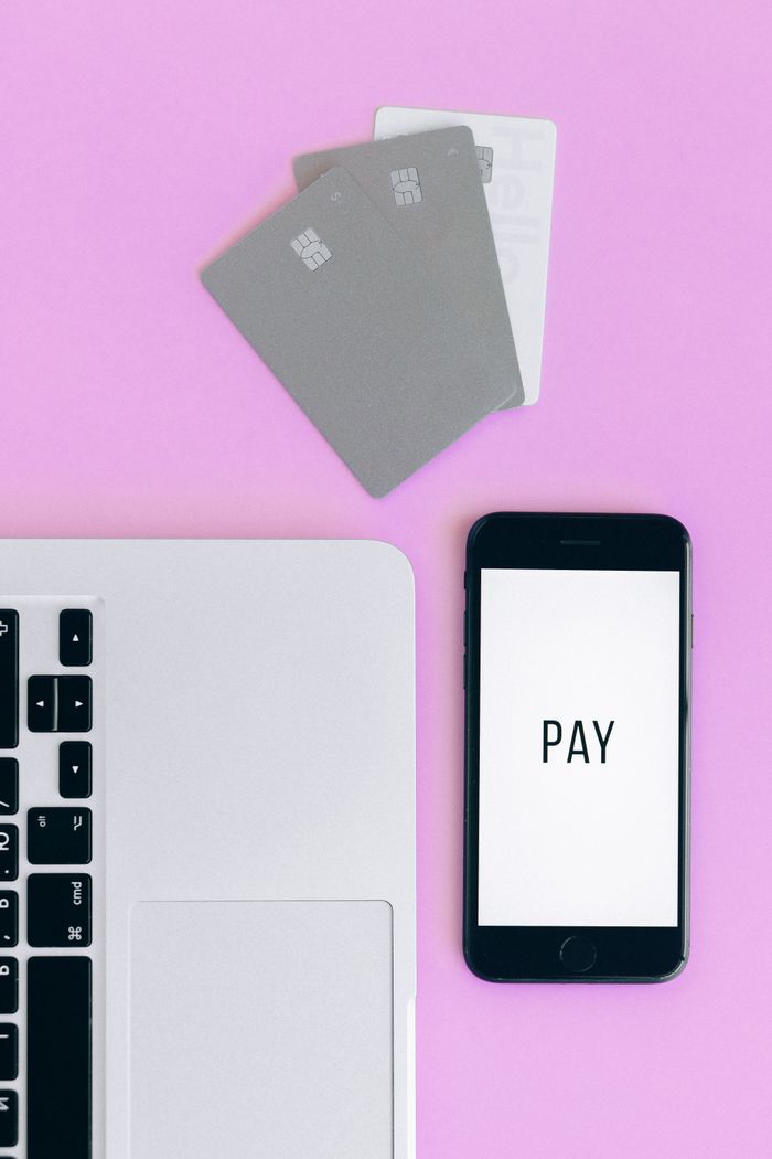 gallery-1 Vue de dessus d'une configuration de paiement mobile avec smartphone, cartes bancaires et ordinateur portable sur fond rose.